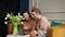 Two cheerful young women sitting on sofa near bouquet of white tulips, looking at grey laptop, laughing shopping online.