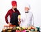 Two chefs in uniform stands near table with vegetable. Chef with assistant in kitchen ready to cook. Professional