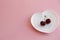 two cherries on a sprig on a white plate in the form of a heart on a light background