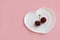 two cherries on a sprig on a white plate in the form of a heart on a light background