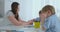 Two children of boys draw with his mother sitting in the kitchen.