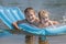 Two children enjoying swimming with inflatable robin egg blue pool air mat in summer pond outdoor