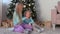 Two children girls sisters playing toys sitting near Christmas tree at home.