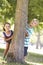 Two Children Hiding Behind Tree In Park