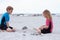 Two children in neoprene swimsuits playing on the beach with sand