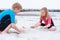 Two children in neoprene swimsuits playing on the beach with sand