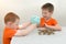 Two children in orange T-shirts on a light background shake coins from a piggy bank. One holds, the other laughs. The idea is that