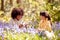 Two Children In Spring Woodlands Examining Bluebells With Magnifying Glass