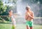 Two childs playing in garden, pours each other from the hose, makes a rain. Happy childhood concept image