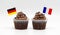 Two chocolate chip swirl cupcakes with tricolor French flag and German flag toothpicks in them isolated on white