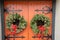 Two Christmas wreaths with bows hanging on an intricate orange door