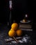 Two cinnamon sticks on icing sugar and a small pyramid of oranges with in the background a bottle of champagne