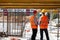 Two civil engineers dressed in orange work vests and helmets discuss the construction process on the building site near