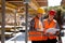 Two civil engineers dressed in orange work vests and helmets explore construction documentation on the building site