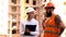 Two civil engineers holding plans and inspecting the construction site. Male and female builder in protective helmets