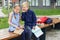 Two classmates read books together and gossip while sitting on bench in school yard. Back to school