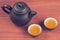 Two clay glazed tea bowls with brewed pu-erh tea and clay teapot on red wooden table vintage filtered