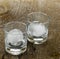 Two clear cocktail glasses on a barn-wood background with large ice sphere inside.