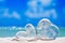 Two clear glass hearts on white sand beach,