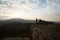 Two climbers standing on summit above clouds in the mountains holding hands. Silhouettes of hikers celebrating ascent on