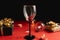 Two clinking wine glasses, various handmade gift boxes decorated with confetti, candle on red and black background.