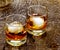 Two cocktail glasses with an amber alcoholic beverage, Rusty Nail, and round ice cubes on a rustic barn wood background.