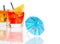 Two cocktail with orange slice on top isolated behind blue umbrella on white background