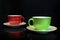 Two coffee cups, green and red ceramic, on black background