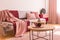 Two coffee cups on wooden coffee table next to classy grey settee with pastel pink pillows and burgundy and pastel pink blankets