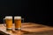 Two cold mugs with beer, with overflowing foam, on wooden table and dark background, space for writing