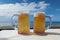 Two cold tankards with beer on the table on the seashore