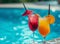 Two colorful cocktails by a sunny pool, one with a red umbrella garnish, evoking a relaxed, tropical vibe.