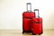 Two colorful red suitcases of same kind different size with telescopic handle up on wooden floor, white wall background. Family tr