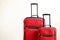 Two colorful red suitcases of same kind different size with telescopic handle up on wooden floor, white wall background. Family tr