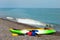 Two colorful sea kayaks with paddles and life jackets on stony b