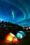 Two colorful sleeping tents under a night sky with green northern lights