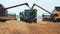 Two combines in a wheat field unload grain into the tractor`s hopper.