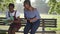 Two confident intelligent African American women sitting on bench in summer park with laptop tablet and paperwork