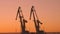 Two construction cranes are working in the port at sunset