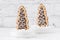 Two cookies shaped as christmas trees with chocolate and sugar glaze in bowls with coarse sugar on white