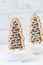 Two cookies shaped as christmas trees with chocolate and sugar glaze in bowls with coarse sugar on white background