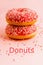 Two coral donuts standing in a line. Donuts decorated with icing