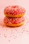 Two coral donuts standing in a line. Donuts decorated with icing