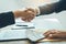 Two corporate businessmen shaking hands while one man places money on document in office room with corruption concept