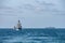 Two corvette warships sail together in the sea with container ship on the horizon