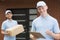 Two couriers in blue uniforms standing in front of a house and waiting with delivery