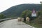 Two cows with bells on their necks walking slowly down a mountain road, passing a traffic slippery road warning sign