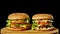 Two craft beef burgers on wooden table isolated on dark grayscale background.