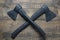 Two crossed black axes on wooden background, top view, closeup