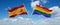 two crossed flags LGBT Pride and spain waving in wind at cloudy sky. Concept of relationship, dialog, travelling between two